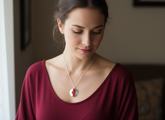 Woman wearing a necklace with a red and silver pendant in a blurred indoor setting