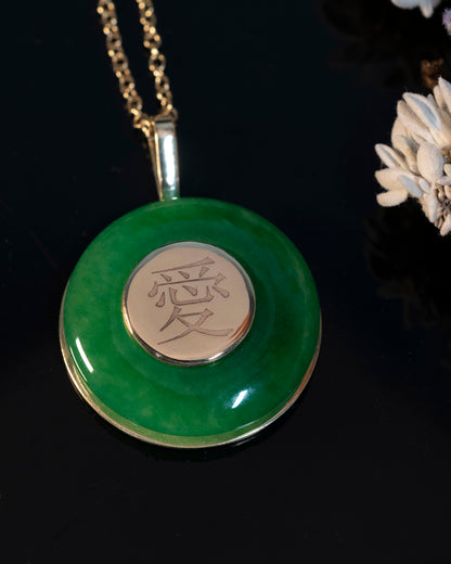A round green jade pendant with a traditional Chinese symbol for love engraved on it, suspended from a gold chain.
