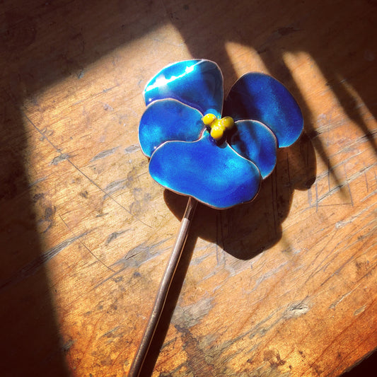 Close-up of the blue enamel pansy detail on the metal hair stick.
